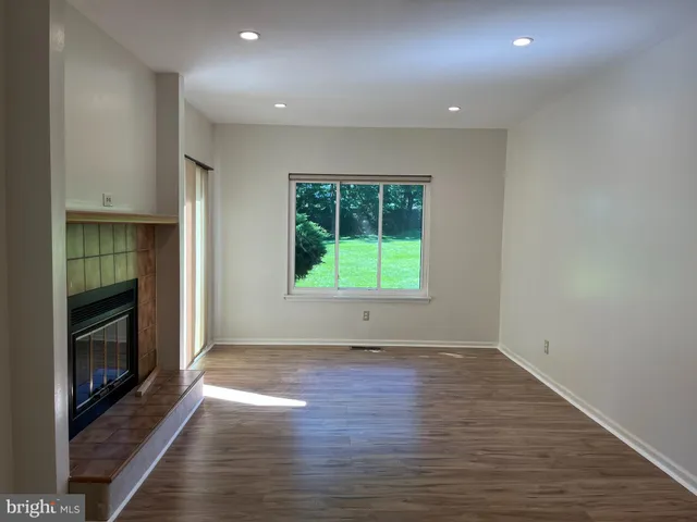 a view of an empty room with wooden floor fireplace and a window