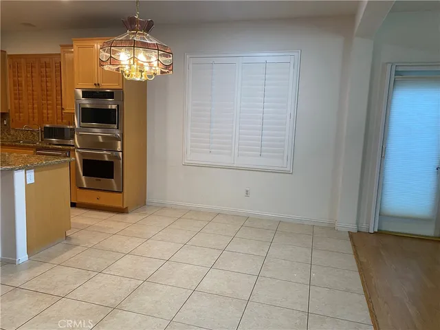 an empty room with chandelier fan and kitchen view