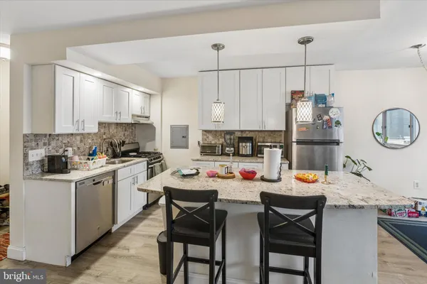 a kitchen with stainless steel appliances kitchen island granite countertop a sink a stove a dining table and chairs with wooden floor