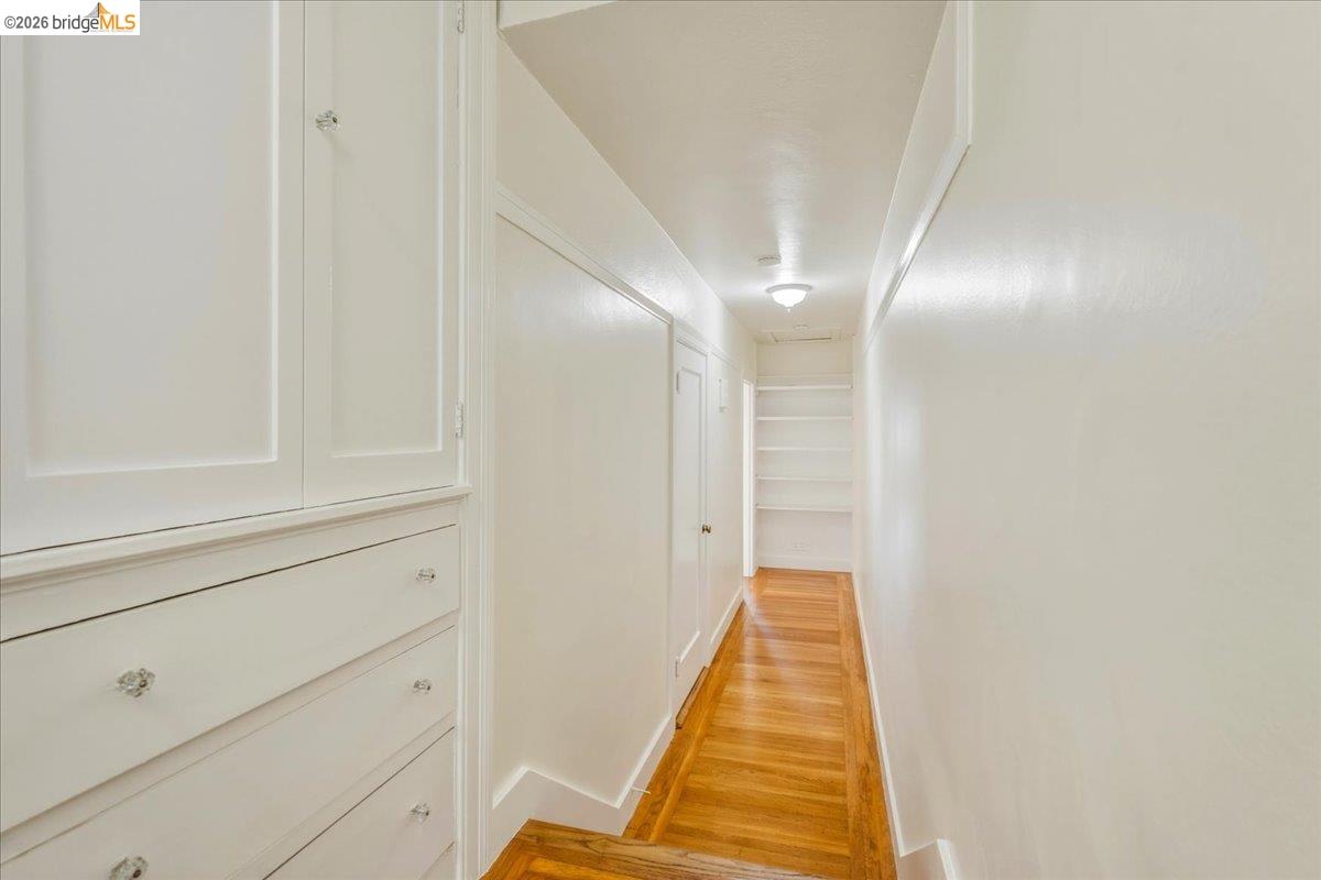 2403 Cedar Street Berkeley, CA 94708 - Photo 28 of 33 Hallway featuring wood-finish flooring, built-in cabinetry with crystal knobs, integrated shelving, white trim, and a flush-mount ceiling light fixture
