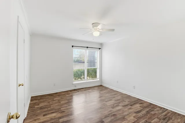 an empty room with wooden floor ceiling fan and windows