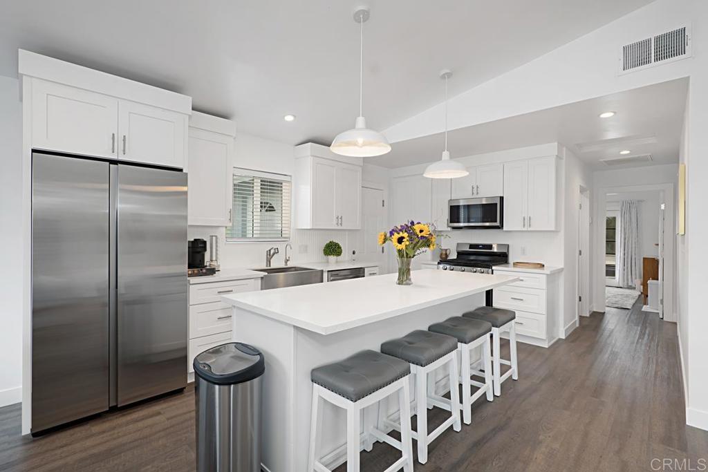 a kitchen with stainless steel appliances a stove a sink a refrigerator white cabinets and wooden floor
