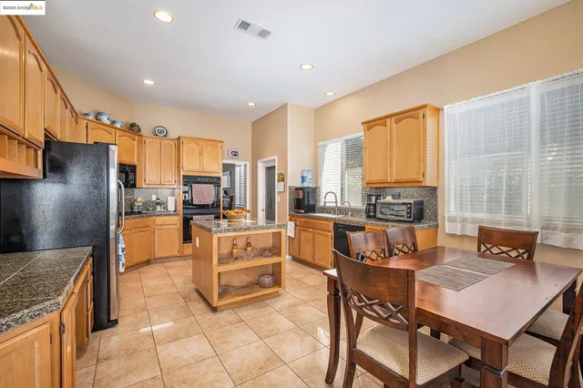 a kitchen with stainless steel appliances granite countertop a stove a refrigerator a kitchen island a table and chairs