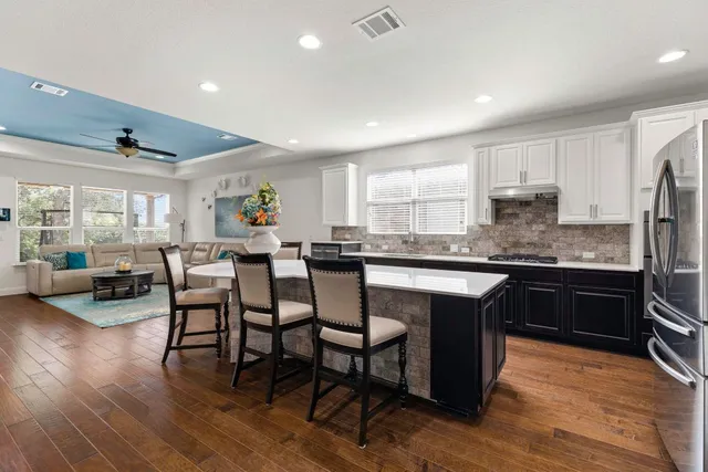 a living room with stainless steel appliances furniture wooden floor and a kitchen view