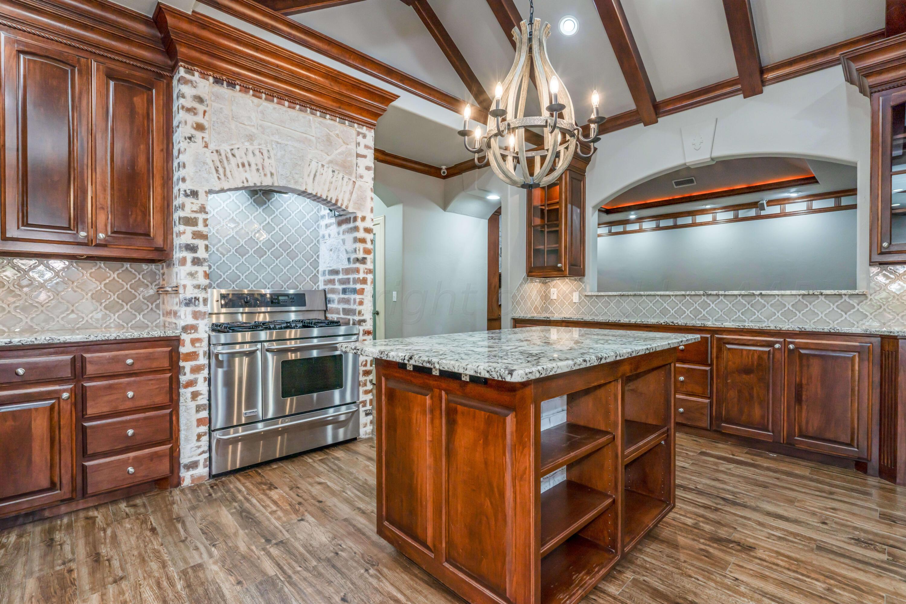 7606 Bayswater Road Amarillo, TX 79119 - Photo 32 of 65 a kitchen with kitchen island granite countertop a stove and a wooden floors