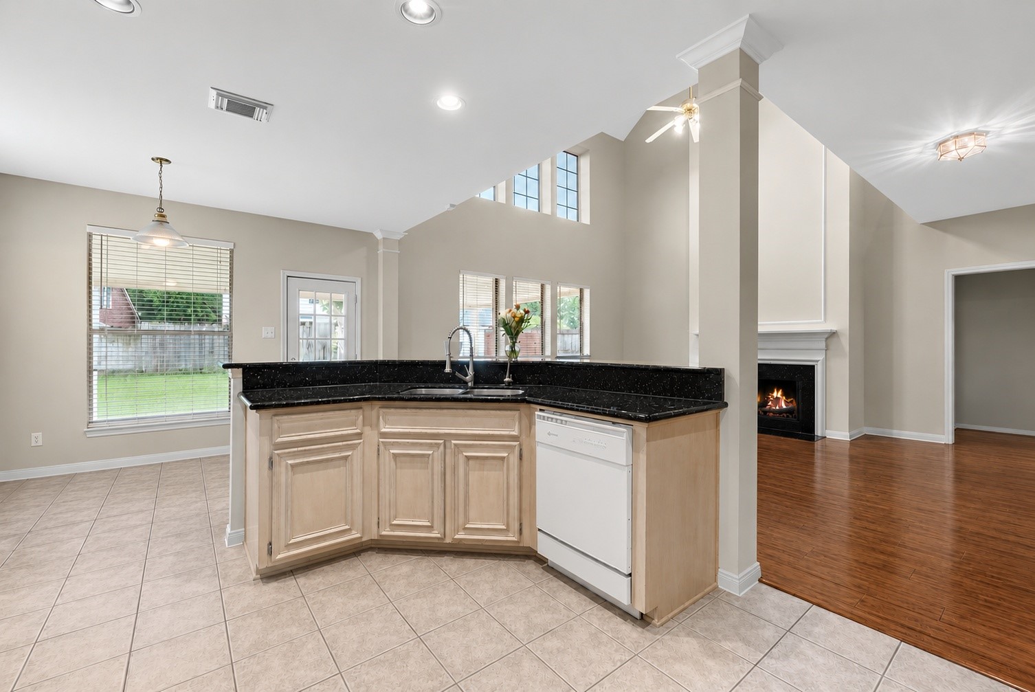 5724 Shady Hollow Court Rosharon, TX 77583 - Photo 8 of 27 Open-concept kitchen and living area featuring soaring ceilings, abundant natural light, and a seamless flow into the main living space with fireplace. The kitchen offers granite countertops, ample cabinetry, a breakfast/dining area nearby, and views toward the backyard, creating a functional layout for everyday living and entertaining. Water filtration system at the sink included.
