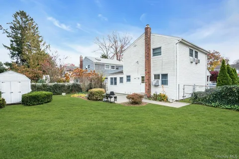 a backyard of a house with table and chairs plants and large tree