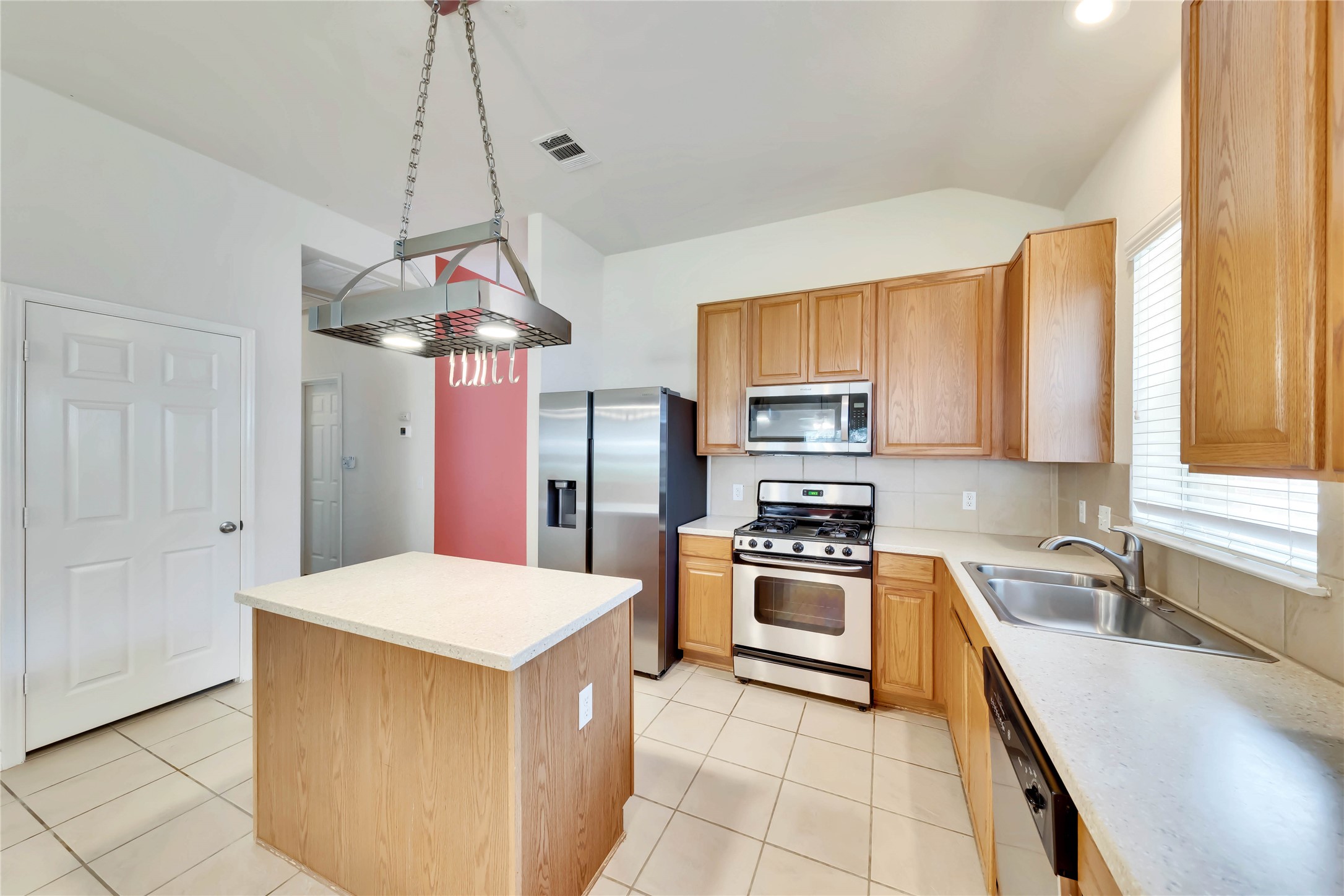 2133 Paradise Ridge Drive Round Rock, TX 78665 - Photo 5 of 22 Kitchen featuring a central island with countertop, light wood cabinetry, white tile flooring, and stainless steel appliances including a gas range, microwave, and refrigerator