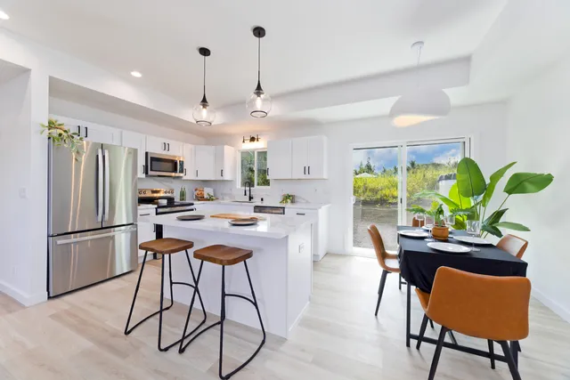 a kitchen with stainless steel appliances granite countertop a refrigerator a sink dishwasher a dining table and chairs with wooden floor