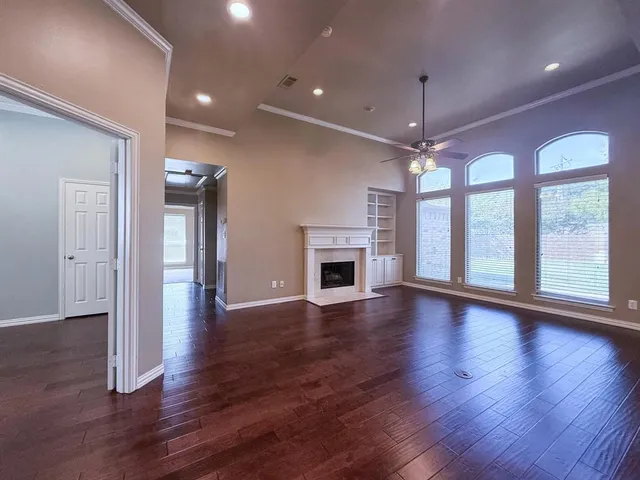 an empty room with wooden floor fireplace and windows
