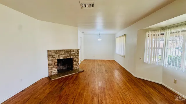 an empty room with wooden floor fireplace and windows