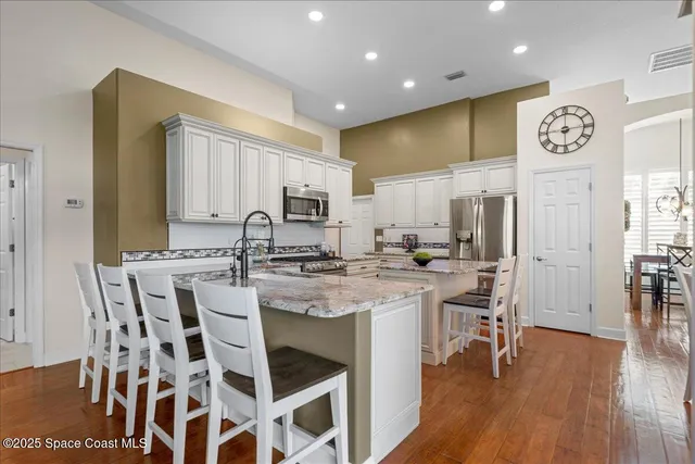 a kitchen with stainless steel appliances kitchen island granite countertop a table chairs cabinets and wooden floor