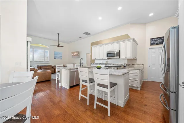 a kitchen with stainless steel appliances a stove a sink dishwasher a refrigerator with white cabinets and wooden floor