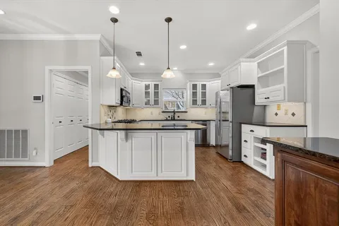 a kitchen with stainless steel appliances kitchen island granite countertop a refrigerator a oven a sink and white cabinets with wooden floor