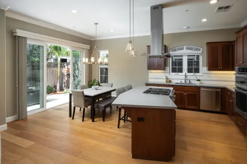 a kitchen with stainless steel appliances granite countertop a stove top oven a sink dishwasher a dining table and chairs with wooden floor