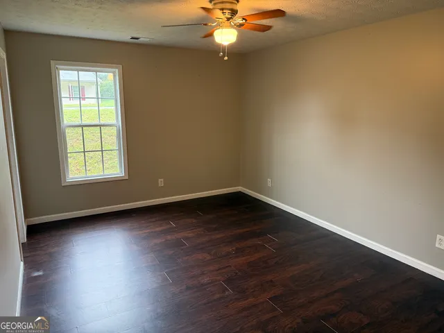 an empty room with wooden floor chandelier fan and windows