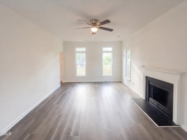 an empty room with wooden floor fireplace and windows