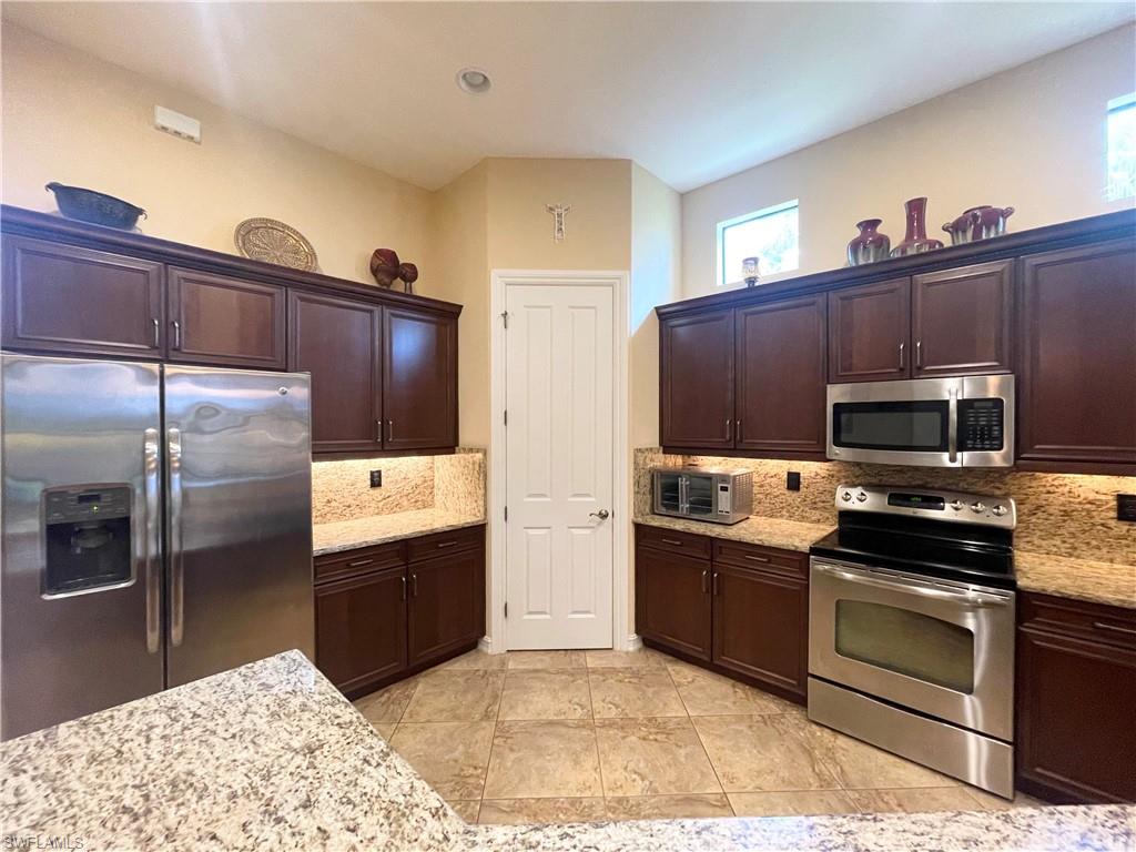 7302 Acorn Way Naples, FL 34119 - Photo 13 of 40 a kitchen with stainless steel appliances kitchen island granite countertop a refrigerator and a stove top oven