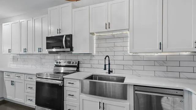 a kitchen with stainless steel appliances granite countertop white cabinets a sink a stove and dishwasher