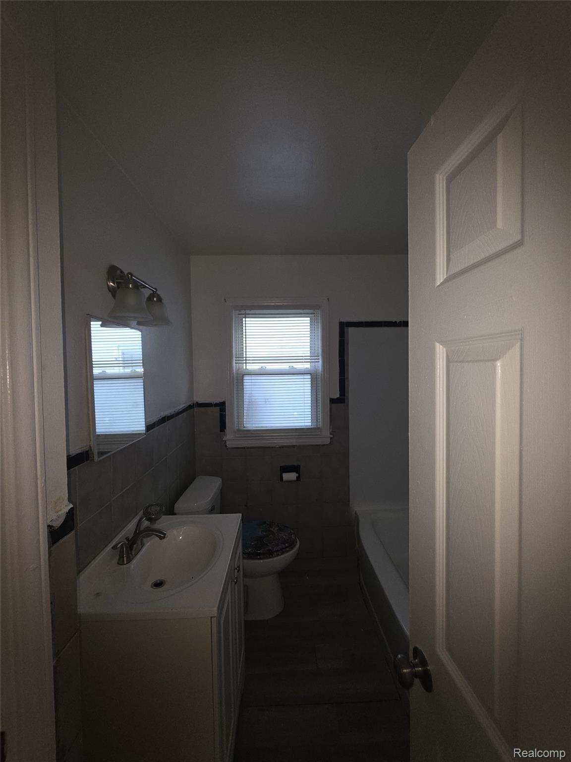 9025 Burt Road Detroit, MI 48228 - Photo 7 of 12 Bathroom featuring a white vanity with integrated sink, chrome faucet, wall-mounted mirror, and ceramic wall tile with dark trim
