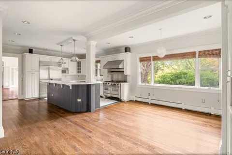 a kitchen with stainless steel appliances kitchen island granite countertop a stove a sink a refrigerator and white cabinets with wooden floor