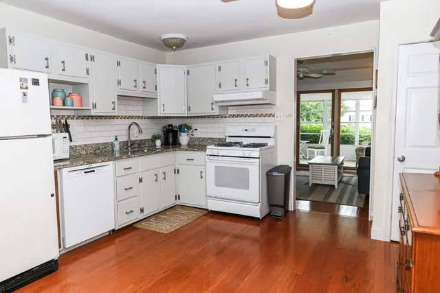 a kitchen with granite countertop a stove a sink dishwasher and white cabinets with wooden floor