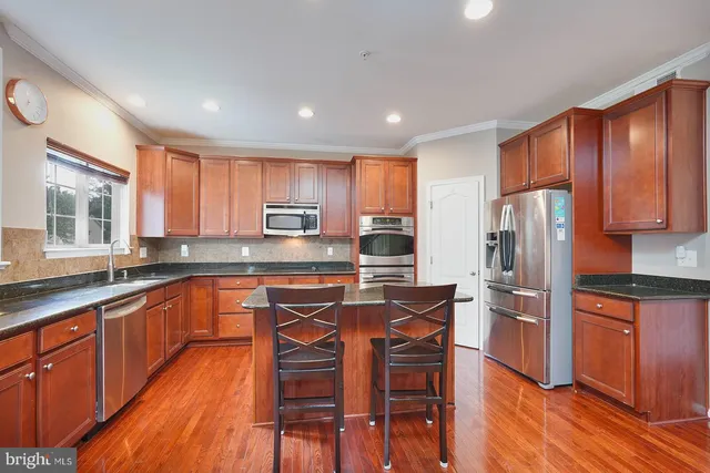 a kitchen with stainless steel appliances wooden floors wooden cabinets and a refrigerator