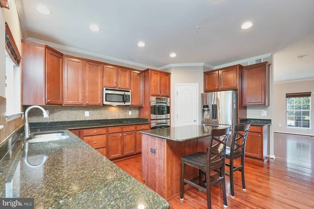 a kitchen with stainless steel appliances granite countertop a stove top oven a sink dishwasher a dining table and chairs with wooden floor