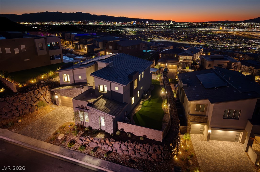 526 Riley Ridge Henderson, NV 89012 - Photo 9 of 10 Dramatic night aerial captures modern residences with city light panoramas, showcasing elegant landscaping and exterior lighting.