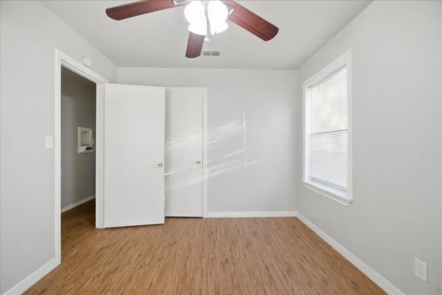 an empty room with wooden floor chandelier fan and windows