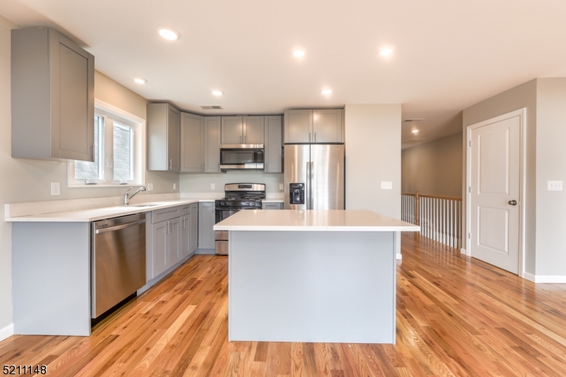 a kitchen with kitchen island wooden floors white cabinets appliances and a window