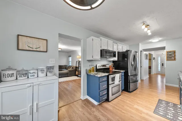 a kitchen with stainless steel appliances granite countertop a stove top oven a sink a refrigerator white cabinets and wooden floor