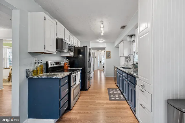 a kitchen with stainless steel appliances granite countertop a stove top oven a sink a refrigerator and white cabinets