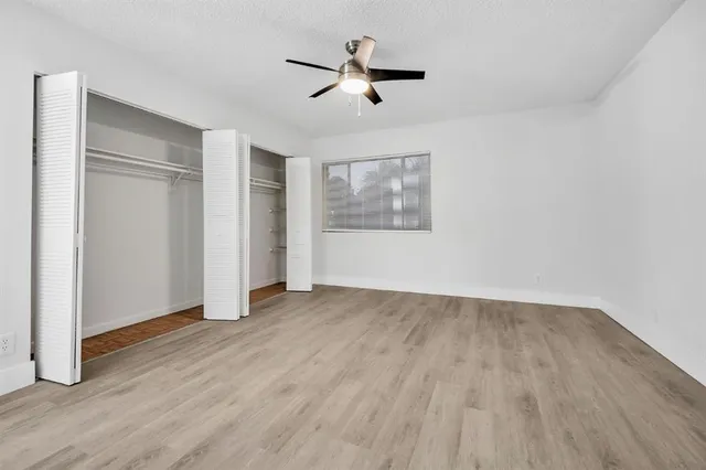 an empty room with wooden floor chandelier fan and windows