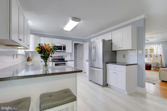 a kitchen with stainless steel appliances granite countertop a refrigerator a sink dishwasher and white cabinets with wooden floor