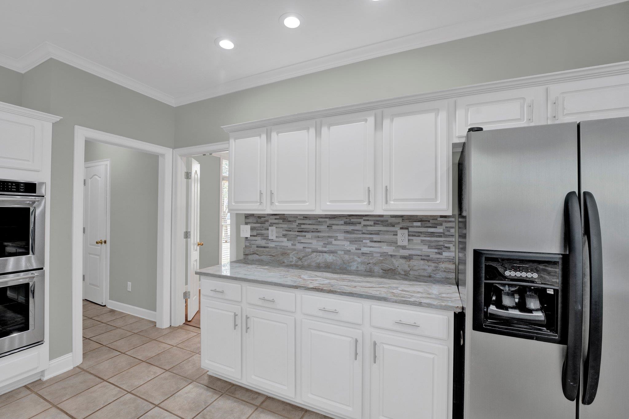 1331 Riding Brook Drive Collierville, TN 38017 - Photo 38 of 39 Kitchen with light tile patterned floors, white cabinets, appliances with stainless steel finishes, decorative backsplash, and ornamental molding