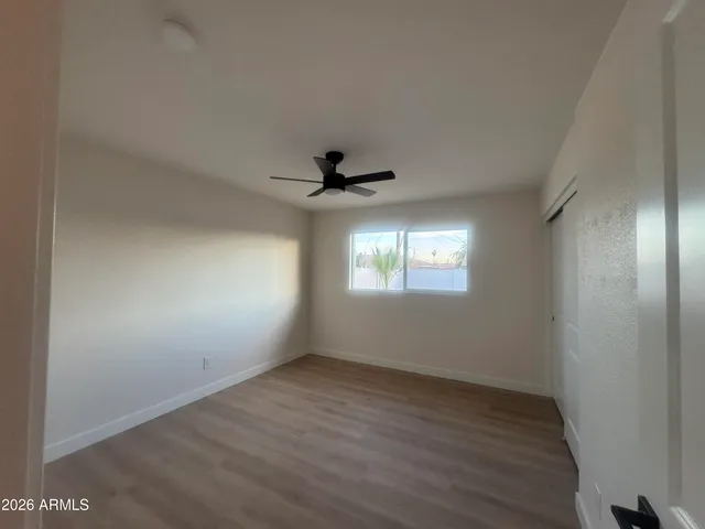 an empty room with wooden floor ceiling fan and windows