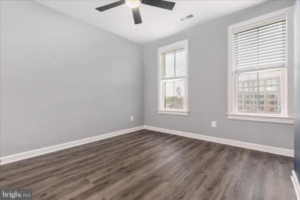 an empty room with wooden floor chandelier fan and windows