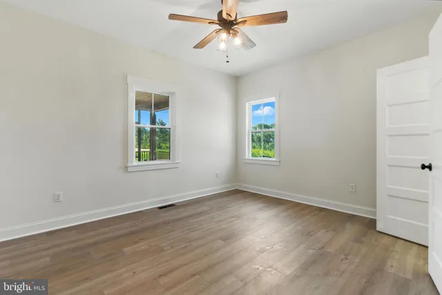an empty room with wooden floor chandelier fan and windows