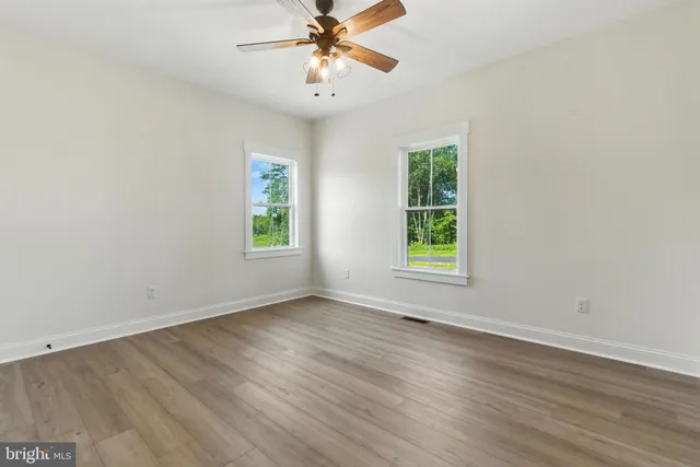 an empty room with wooden floor chandelier fan and windows