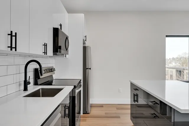 a kitchen with stainless steel appliances a sink dishwasher a stove top oven a refrigerator with wooden cabinets and floor