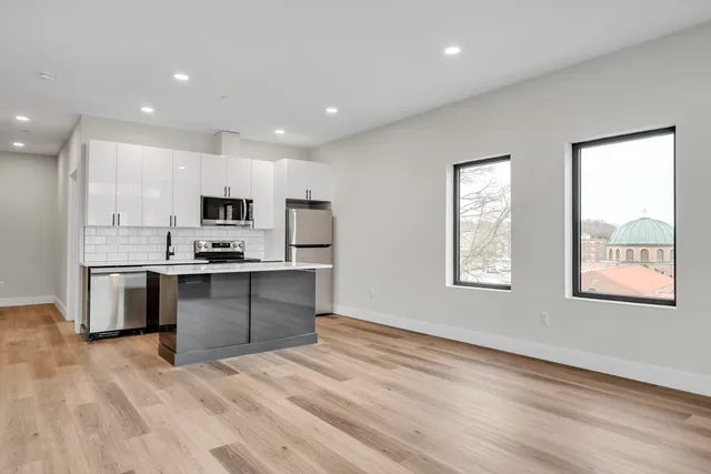 a open kitchen with stainless steel appliances granite countertop a stove top oven a sink dishwasher a refrigerator and white cabinets with wooden floor