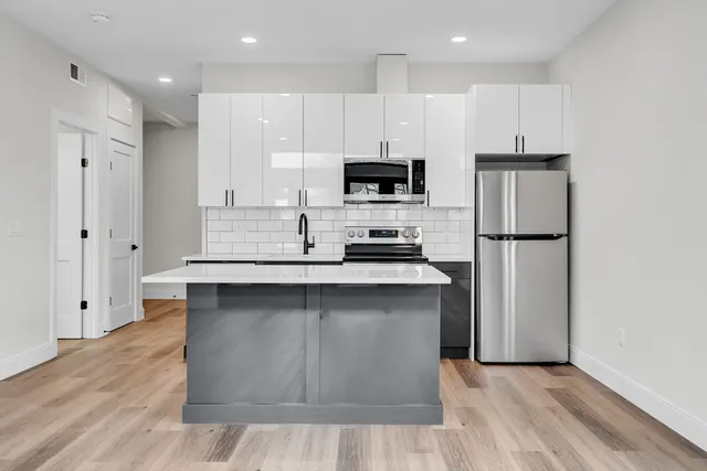 a kitchen with stainless steel appliances granite countertop a refrigerator a stove a sink and white cabinets with wooden floor