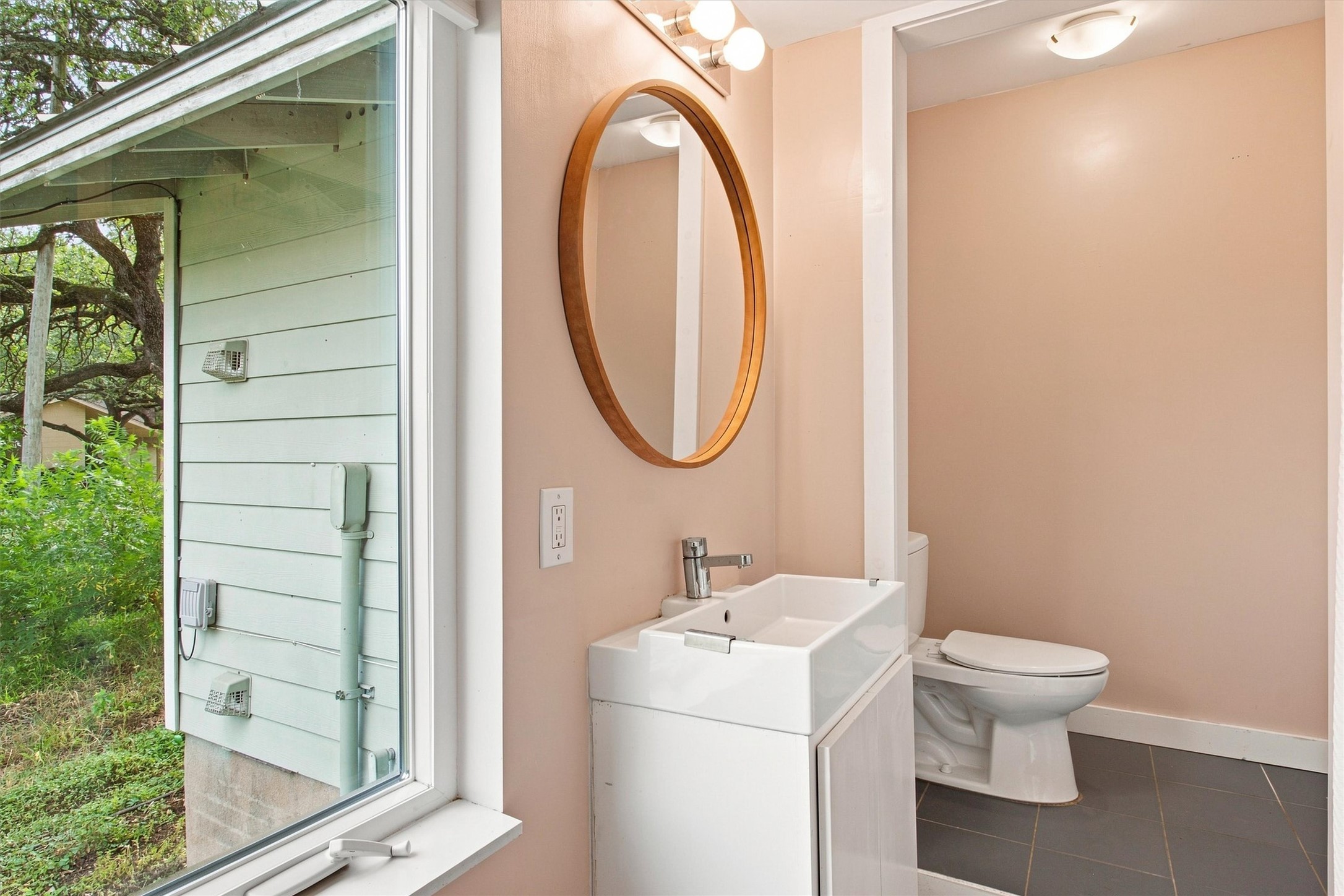 7200 Albert Road Austin, TX 78745 - Photo 12 of 17 A well-appointed powder room features a modern basin, a toilet, and a circular mirror, offering a contemporary aesthetic.