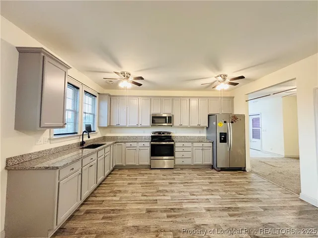 a kitchen with stainless steel appliances granite countertop a stove top oven a sink a refrigerator and white cabinets