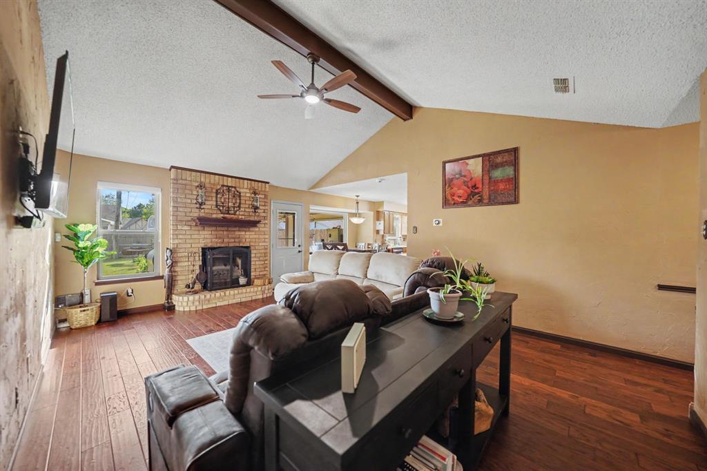 7624 Maple Hill Road Watauga, TX 76148 - Photo 8 of 20 Vaulted ceiling with exposed wood beam, brick fireplace with mantel, wood-finish flooring, and a ceiling fan with integrated lighting