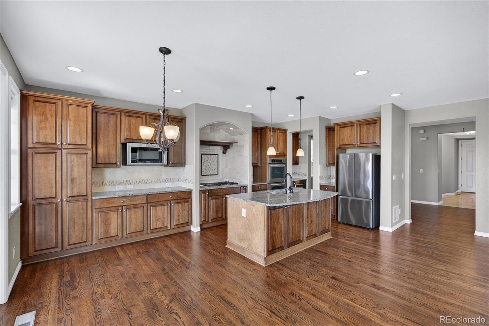 10872 Valleybrook Circle Highlands Ranch, CO 80130 - Photo 14 of 50 a kitchen with stainless steel appliances granite countertop a refrigerator a oven a sink and white cabinets with wooden floor