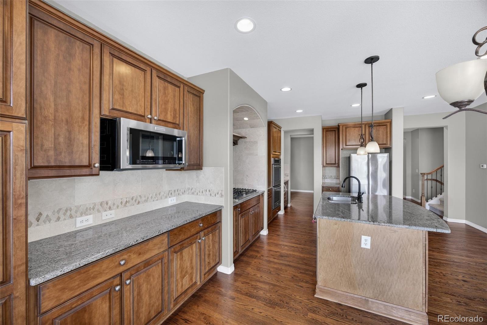 10872 Valleybrook Circle Highlands Ranch, CO 80130 - Photo 16 of 50 a large kitchen with stainless steel appliances a large counter top a stove a sink dishwasher a microwave oven and a dining table with wooden floor