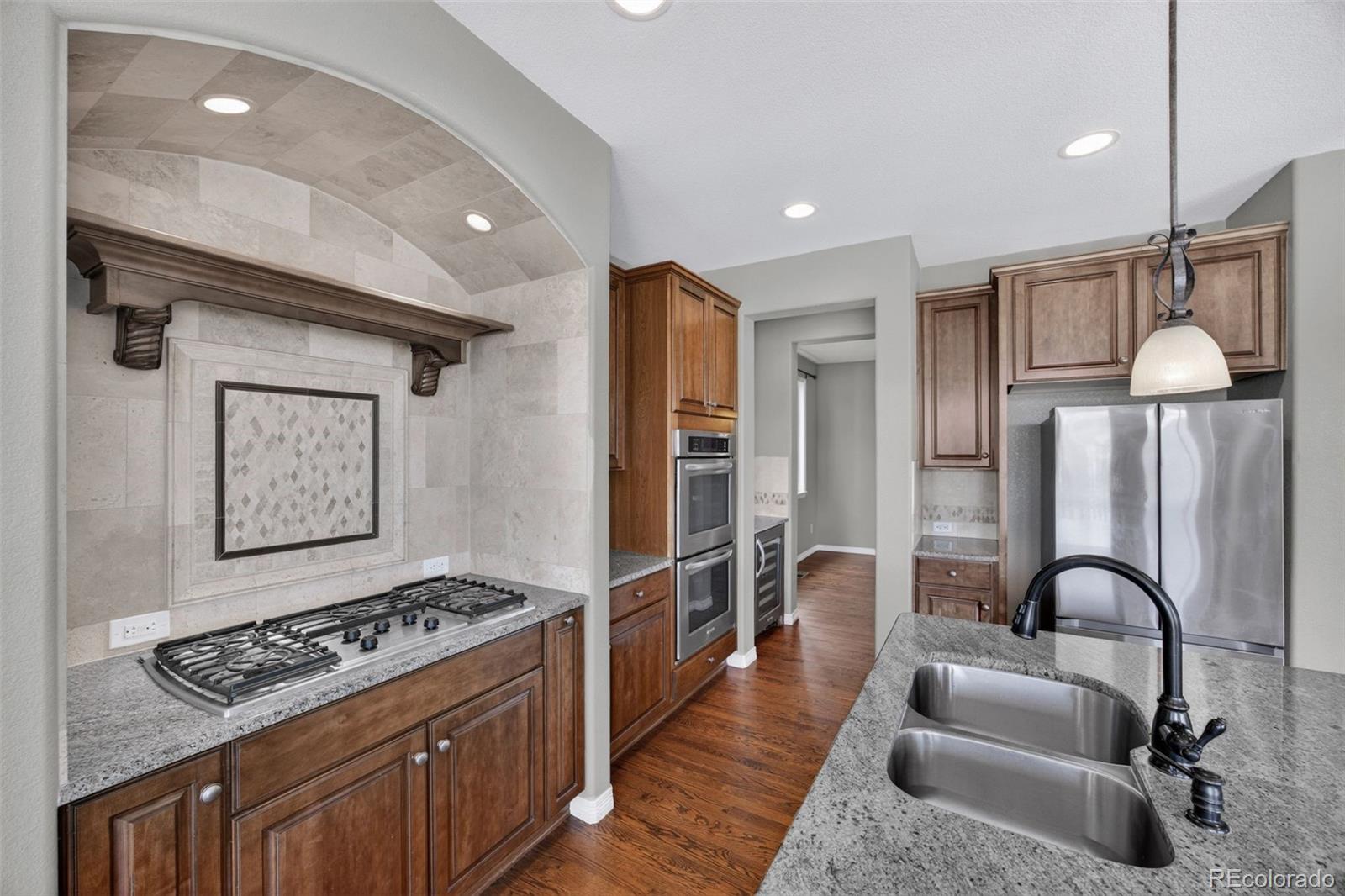 10872 Valleybrook Circle Highlands Ranch, CO 80130 - Photo 17 of 50 a kitchen with stainless steel appliances granite countertop a stove a sink dishwasher and a refrigerator with wooden floor
