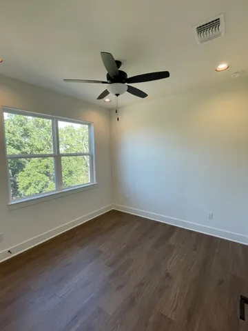 an empty room with wooden floor fan and windows